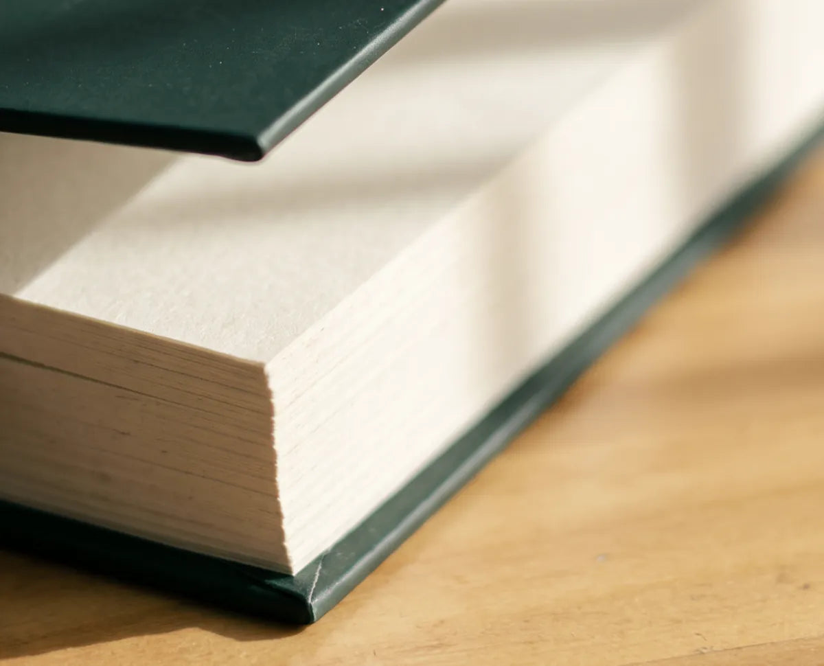El canto de las hojas crema del cuaderno rumbo, con la tapa verde entreabierta sobre una mesa de madera